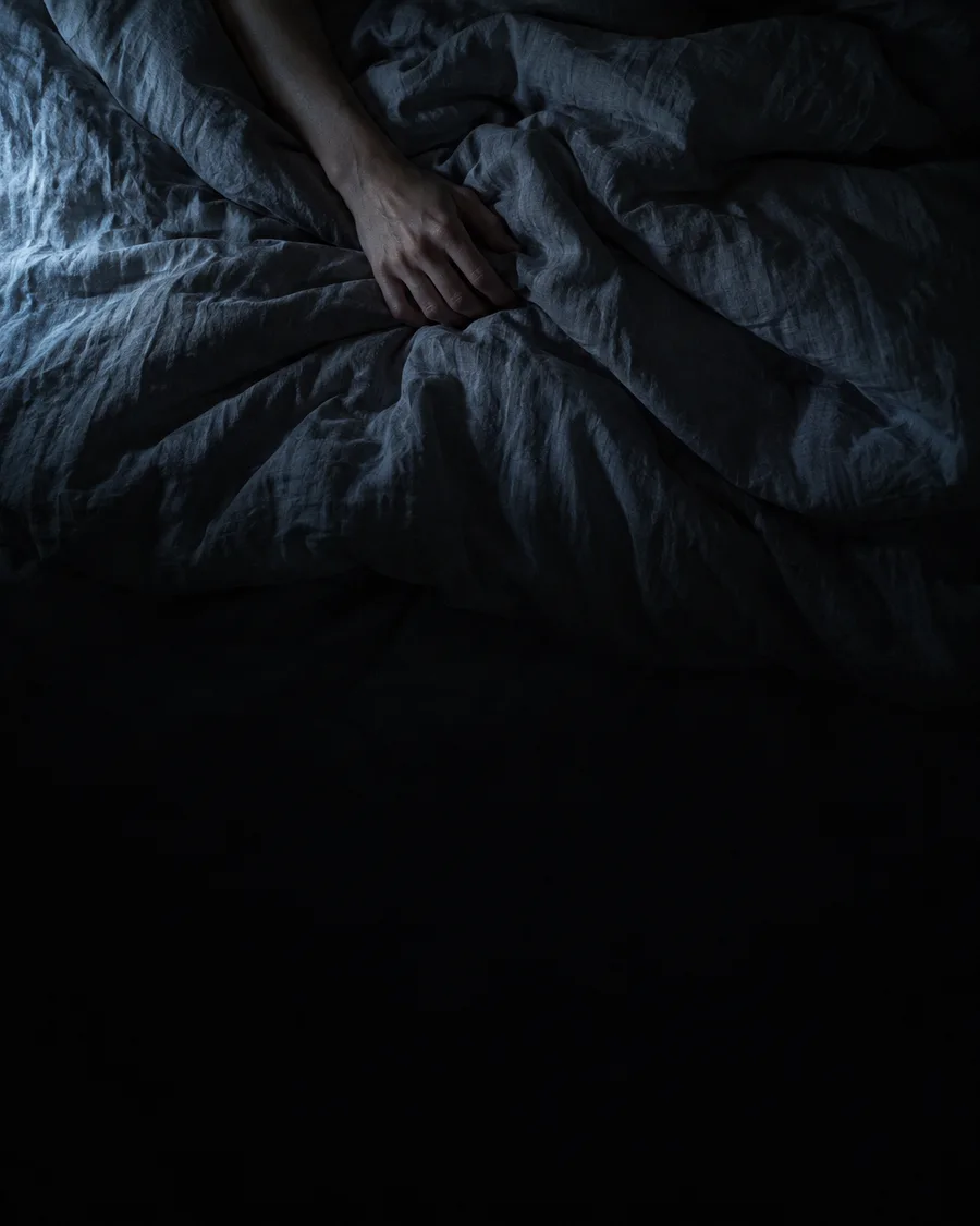 Dunkles Schlafzimmer, eine Hand auf der Bettdecke
